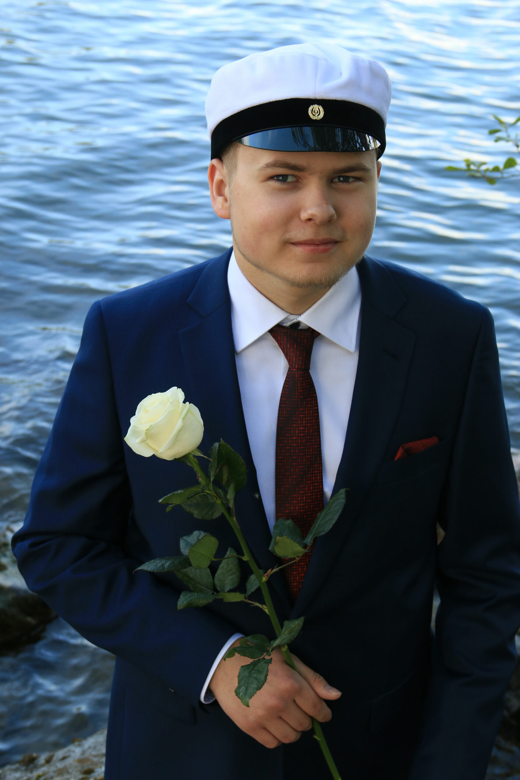 Ylioppilas valkoinen ruusu kädessä järven rannalla